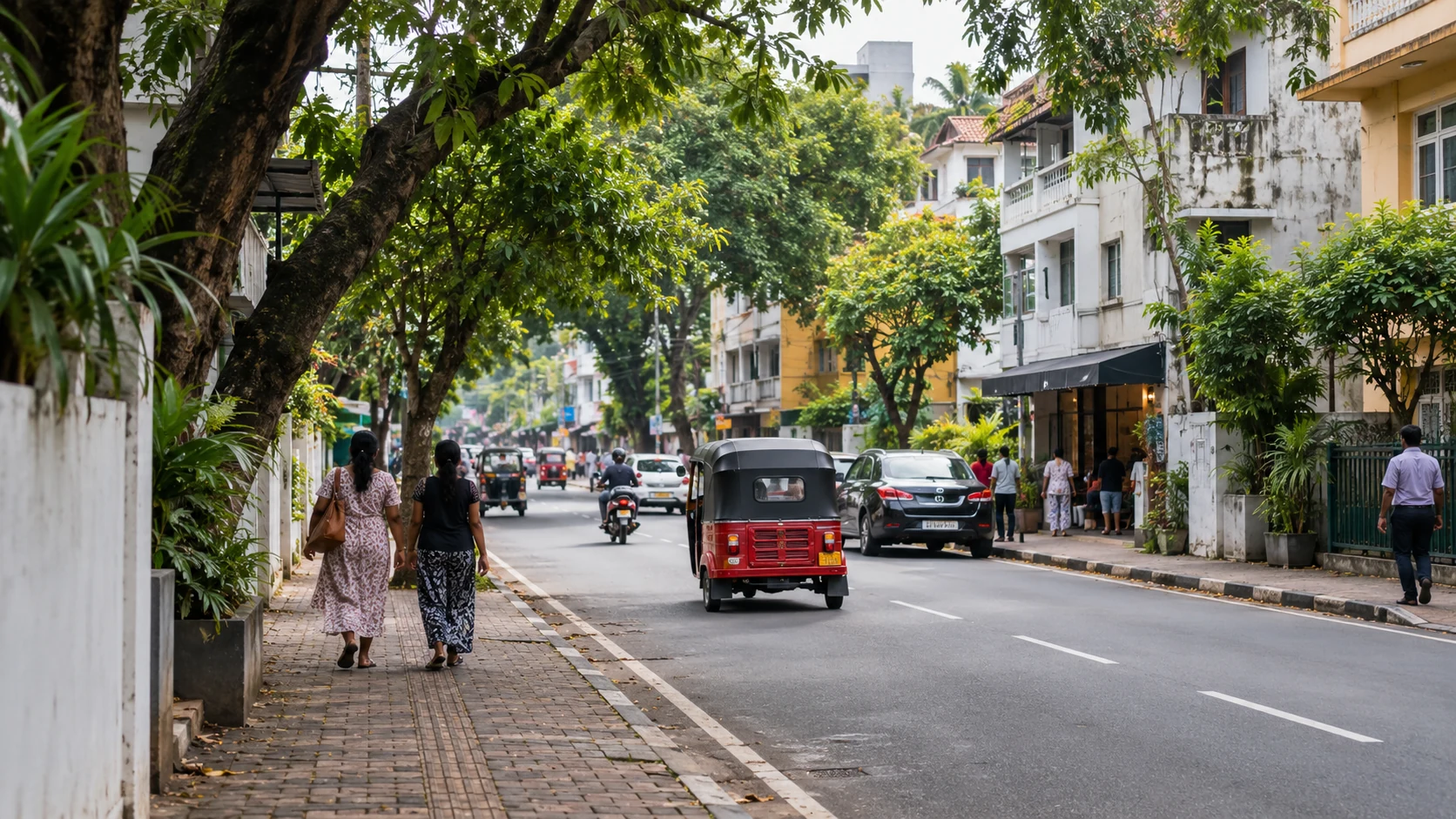 A tree-lined urban street with a tuk-tuk and varied buildings